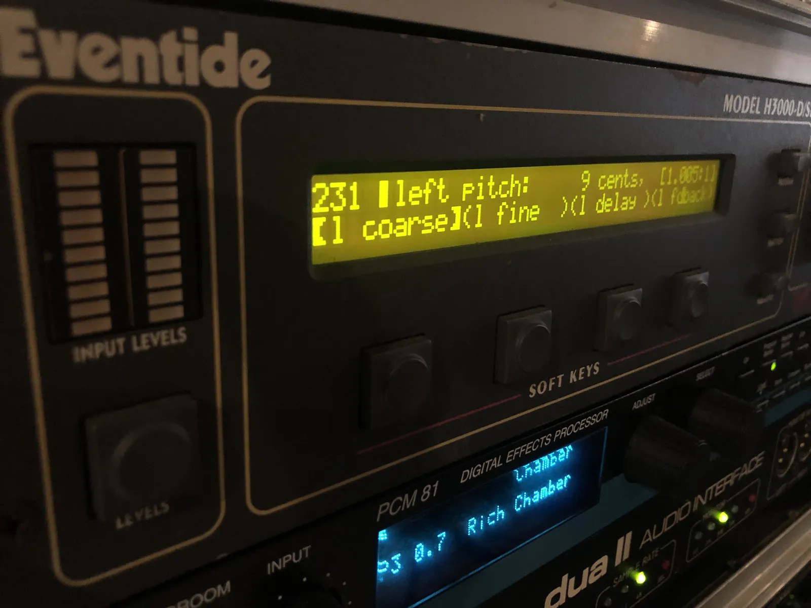 An angled H3000-D/SE front panel view. The yellow-green LCD shows “231 left pitch: 9 cents, [1.005:1]” above the l coarse, l fine, l delay and l fdback soft-key labels. Four soft keys sit below; INPUT LEVELS meters and the LEVELS button are on the left. Other rack equipment is visible beneath.